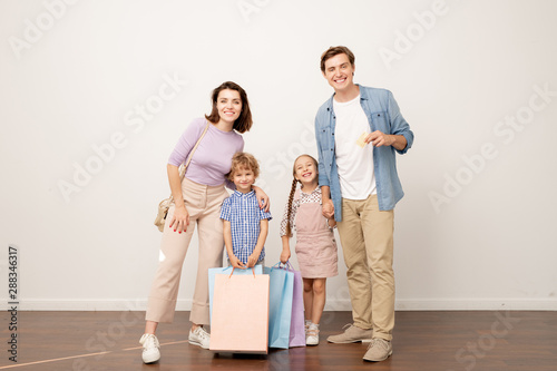 Foto Joyful young parents and their two kids with paperbags looking at you