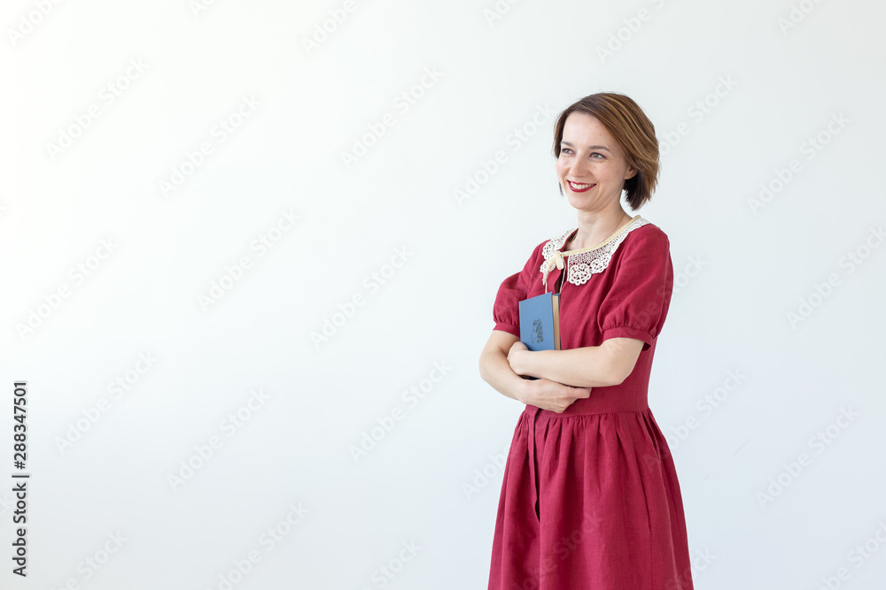 Portrait of cute smiling modest woman in dress holding classic book in hands on white background. Concept of lovers of history and classics. Copy space Portrait of cute smiling modest woman in dress holding classic book in hands on white background. Concept of lovers of history and classics. Copy space