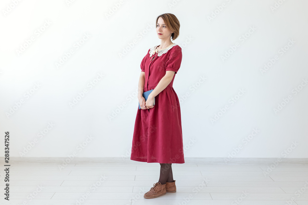 Portrait of cute smiling modest woman in dress holding classic book in hands on white background. Concept of lovers of history and classics. Copy space Portrait of cute smiling modest woman in dress holding classic book in hands on white background. Concept of lovers of history and classics. Copy space