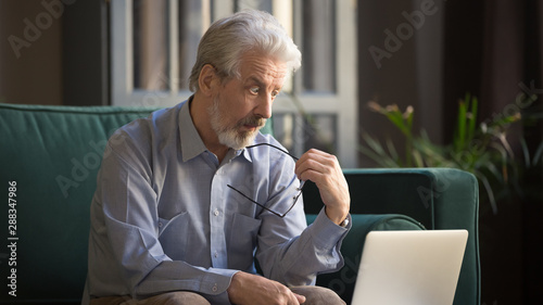 Pensive mature man distracted from computer thinking photo