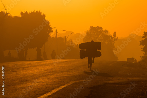 An African/Mozambican cycling to work at sunrise with large bags of coal to sell at market the morning. Nampula Town, Mozambique
