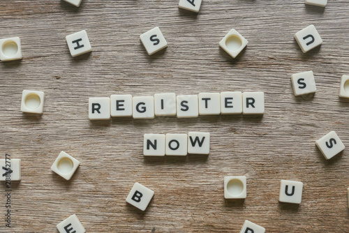 Business and finance concept. Register Now alphabet square on wooden background. photo