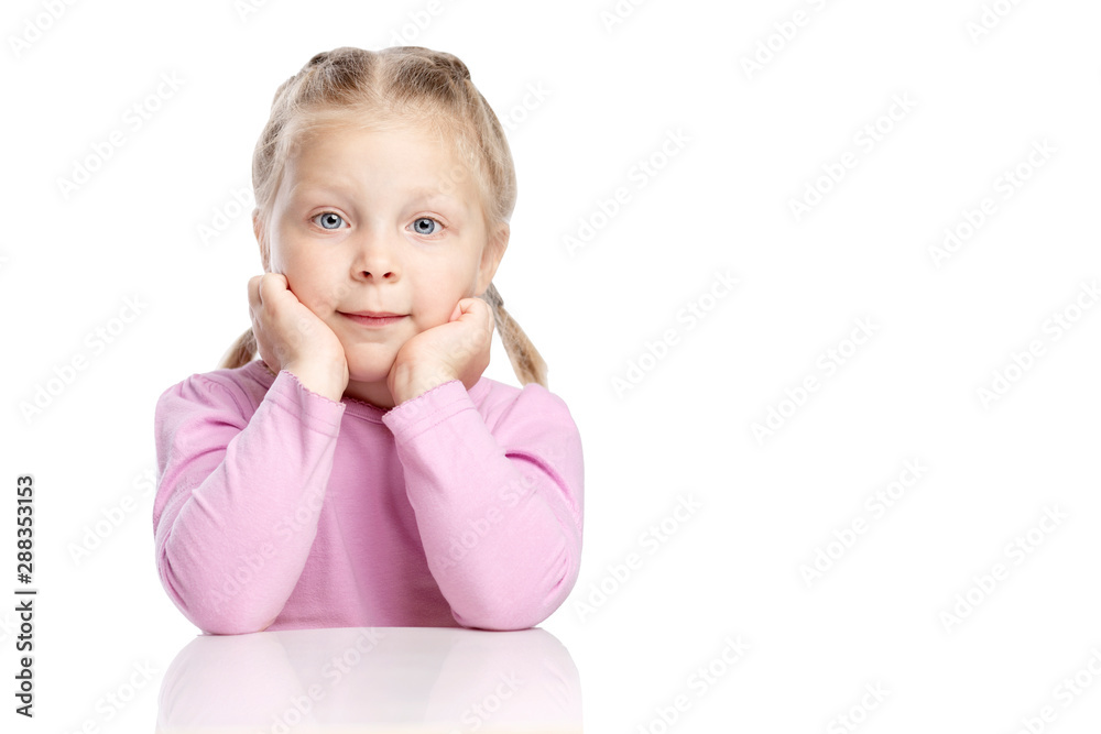 Little pensive girl with pigtails sits at a table and dreams. Poured on a white background. Little pensive girl with pigtails sits at a table and dreams. Poured on a white background.