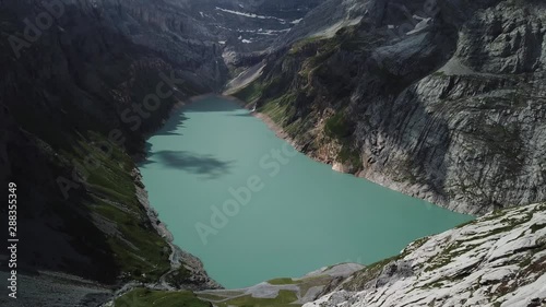Man walking towards the edge of the mountain while hiking in the alps. He is walking towards to the Limmernsee reservoir and dam. In the background can be seen the lake and the alpine mountains. photo