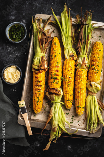 grilled corn on a baking sheet, top view, dark background, rustic style