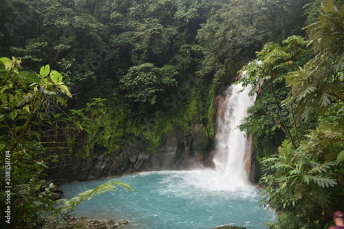 Beautiful waterfall of turquoise blue water, surrounded by green tropical vegetation.