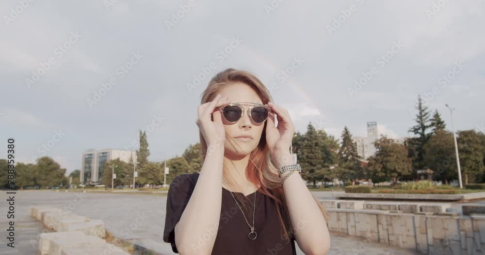Young female model bathed in sunlight puts on stylish sunglasses - rainbow in background Young female model bathed in sunlight puts on stylish sunglasses - rainbow in background