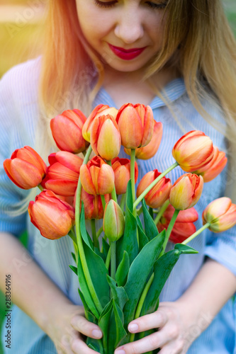 Young pretty caucasian smiling woman is holding a bouquet of red tulips, dating, wedding day, vertical