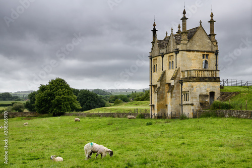 Sheep grazing in field at 17th Century East Banqueting Hall beside St James' church under cloudy sky in Chipping Campden England photo