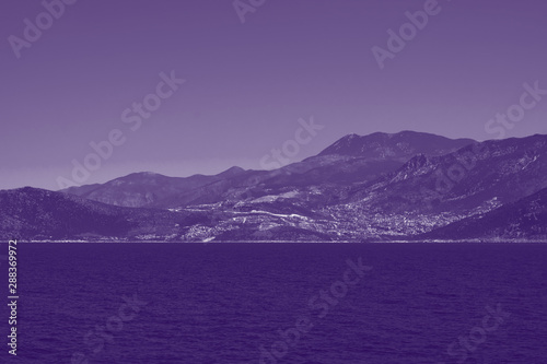 Toned background made of seascape with rocky island, mountains in mist