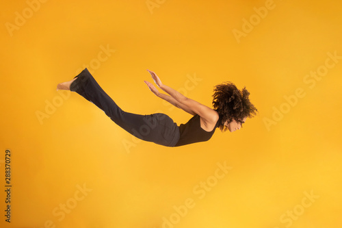 Side view of afro hair woman in zero gravity or a fall. Girl is flying, falling or floating in the air. Side view of person. Over yellow background. Girl flies down jumping from a helicopter.