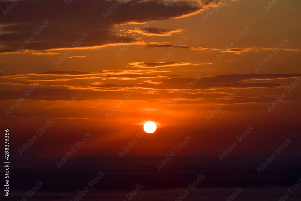 Red sunset sky with clouds over dark foggy landscape. Bright sunny circle in the sky. Natural scenery, beautiful scenery in late evening. Red sunset sky with clouds over dark foggy landscape. Bright sunny circle in the sky. Natural scenery, beautiful scenery in late evening.
