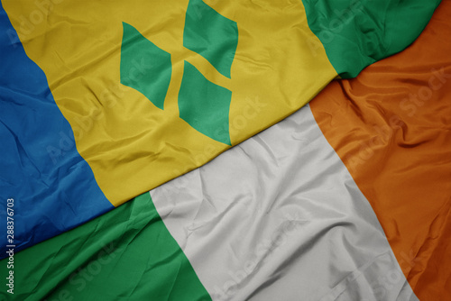 waving colorful flag of ireland and national flag of saint vincent and the grenadines.