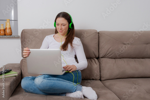 Happy woman using laptop and listening to music on a comfortable sofa.