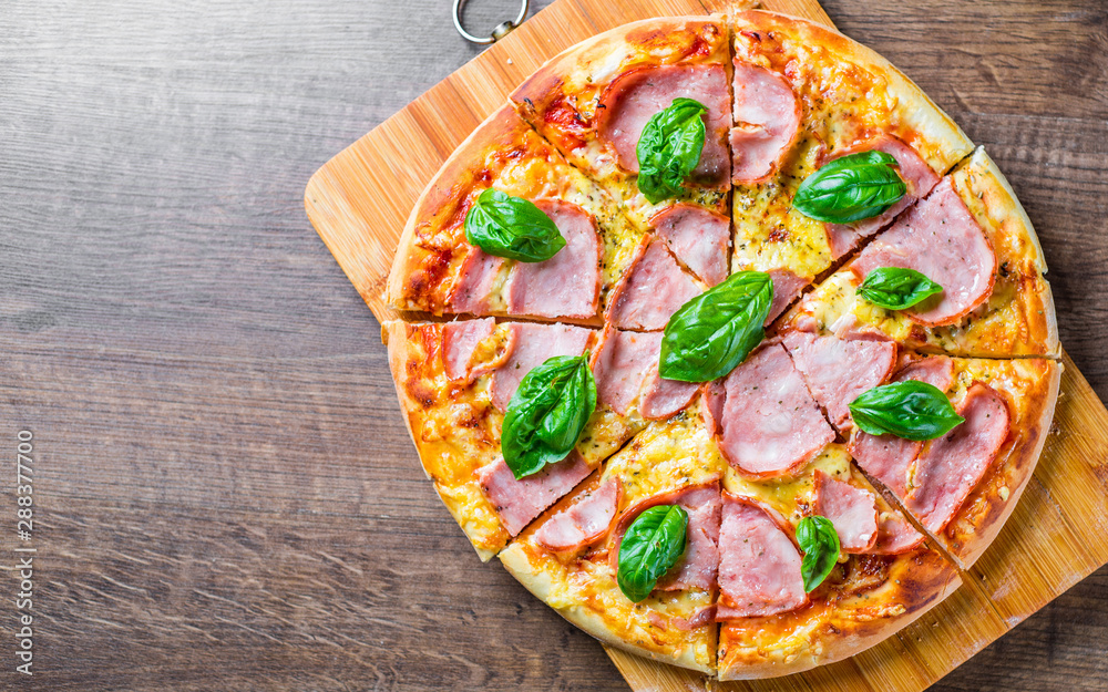 Pizza with Mozzarella cheese, ham, tomato sauce, pepper, Spices and Fresh basil. Italian pizza on wooden table background