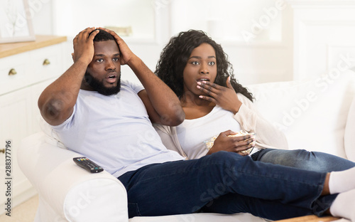 Shocking news. Black married couple watching tv and eating popcorn