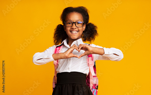 African American Schoolgirl Showing Heart Gesture With Hands In Studio photo