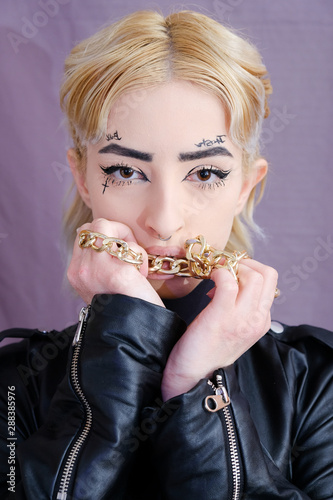 Studio portrait of young woman in leather jacket holding golden chain and touching her lips