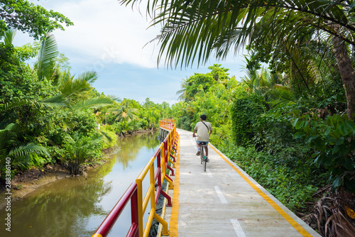 A young man cycles in Bang Krachao (Bang Kachao), along the moat and stilted pathway surrounded by lush tropical vegetation. Bang Krachao is known as the Green Lung of Bangkok. photo