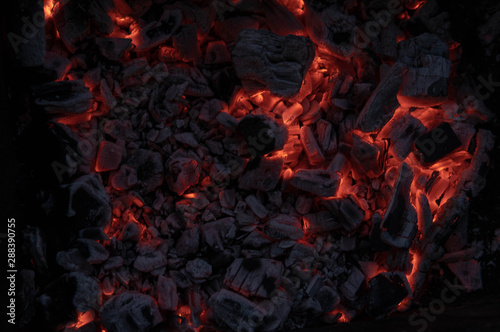 The texture of the coal fire. Actively smoldering embers of fire. Background of burning hot coals. Flicker of burning coals at night