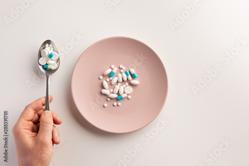 Hand with spoon of pills and plate with pills. Flat lay