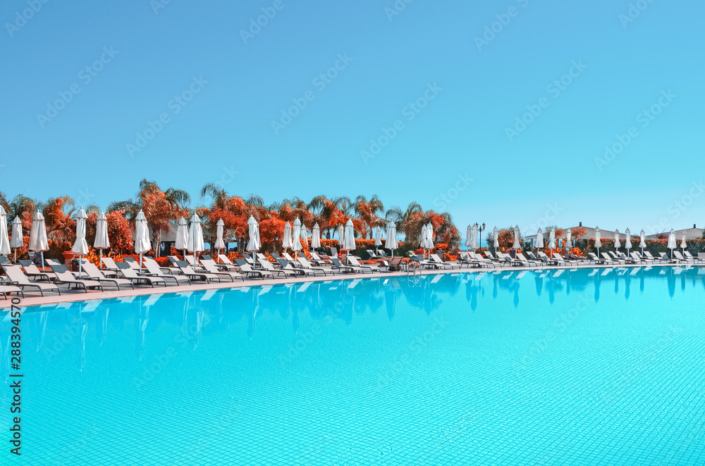 Large open air blue water pool. White sun umbrellas and sun beds around the pool. The concept of rest and relaxation. Pool side.