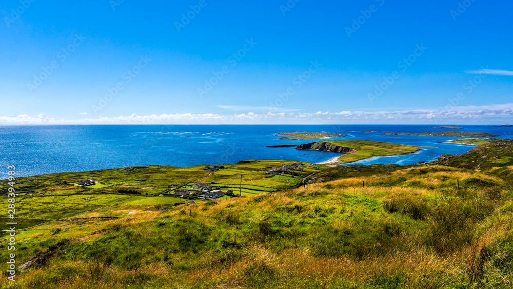 Small village, green fields and meadows on the coast, beautiful coastline and islands, moody blue sky with clouds, Wiled Atlantic Way, Ireland