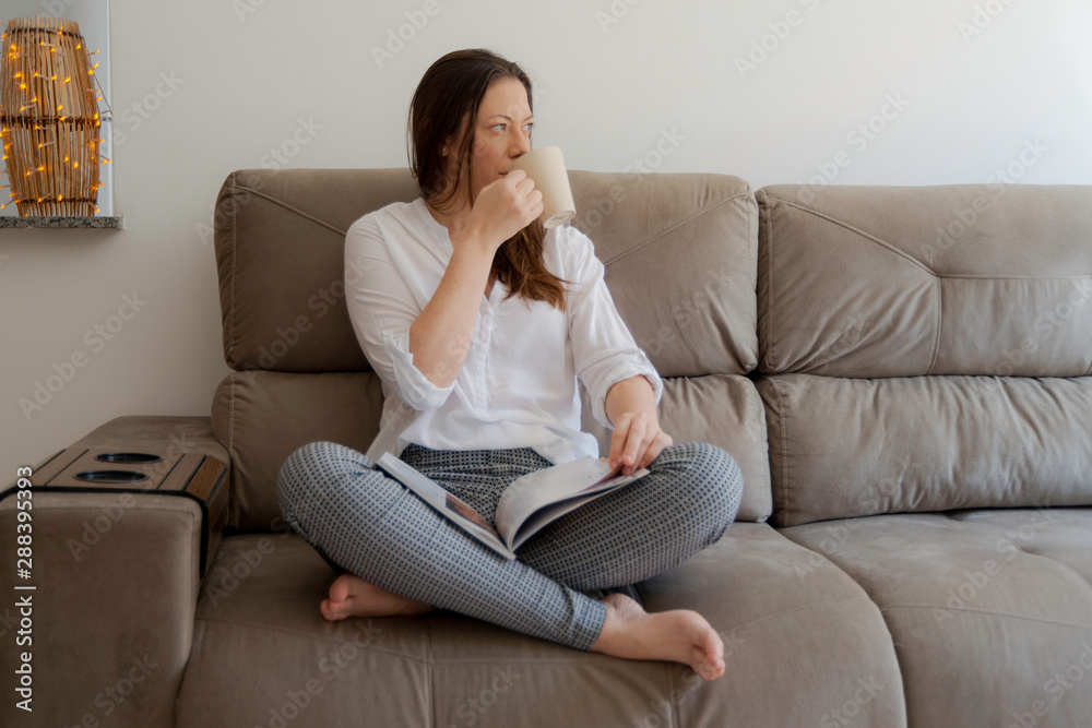 Beautiful woman sitting on the couch reading magazine and having a tea. Beautiful woman sitting on the couch reading magazine and having a tea.