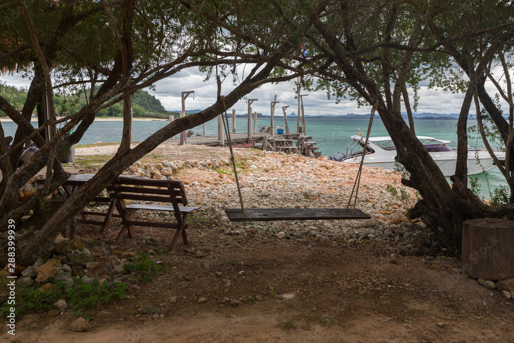 a peaceful resting area with a wooden bench and a traditional swing, near the beach at Koh Talu, Thailand