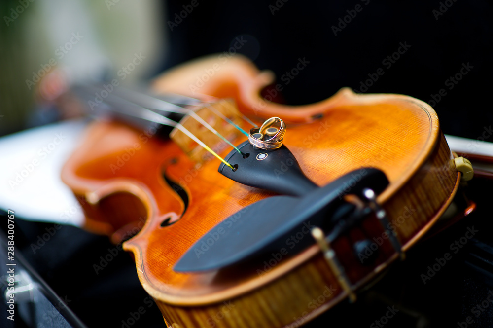 Fototapeta premium wedding rings lie on the edge of the violin with strong bokeh