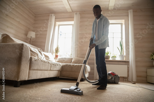 African American man use vacuum cleaner hovering house