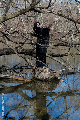 Foto Hooded woman in black robes standing on a tree stump in the middle of a swamp