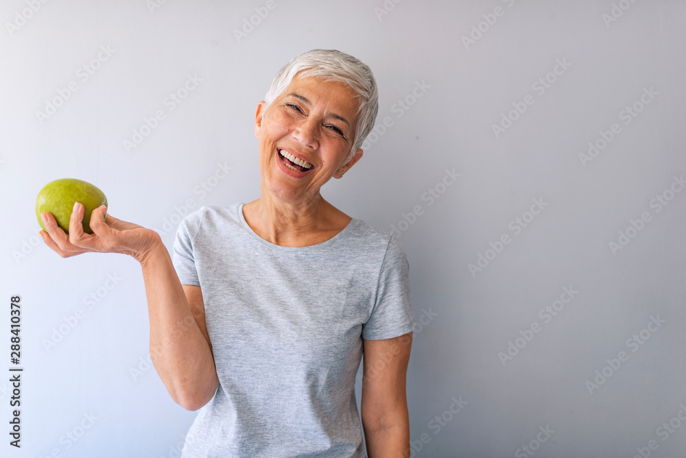 Portrait of a beautiful elderly woman holding an apple, smiling, isolated on gray background. Happy Woman Holding Granny Smith Apple. An aple a day keeps doctor away Portrait of a beautiful elderly woman holding an apple, smiling, isolated on gray background. Happy Woman Holding Granny Smith Apple. An aple a day keeps doctor away