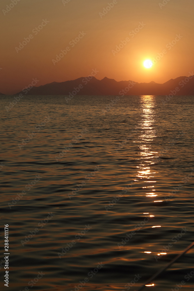 View from the yacht to the sun setting behind the mountains View from the yacht to the sun setting behind the mountains
