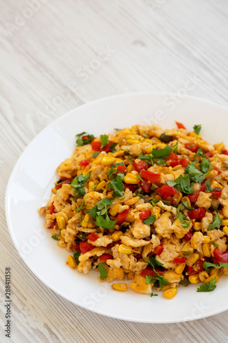 Homemade southwestern egg scramble on a white plate on a white wooden surface, side view. Copy space.