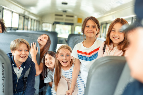 Classmates going to school by bus sitting inside talking to driver cheerful