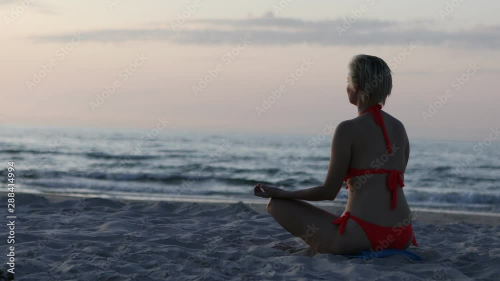 Timelapse: Beautiful blond girl with bikini meditates on the beach while the sun goes down. Timelapse: Beautiful blond girl with bikini meditates on the beach while the sun goes down.