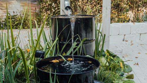 Rain water flows from a drainpipe to the metal barrel in garden in summer close up photo