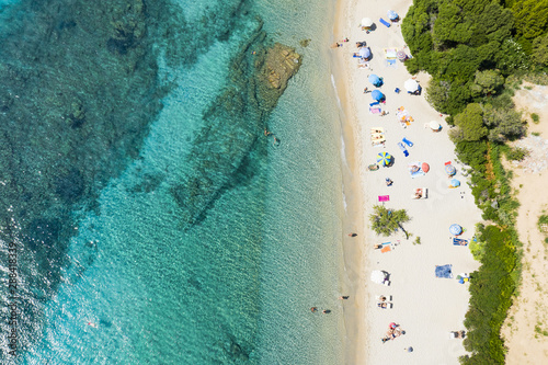 View from above, stunning aerial view of a beautiful beach full of colored beach umbrellas and people swimming in a turquoise clear water. Capriccioli Beach, Costa Smeralda, Sardinia, Italy.