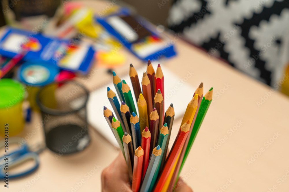 Hand holding color pencils on blurred stationery background Hand holding color pencils on blurred stationery background