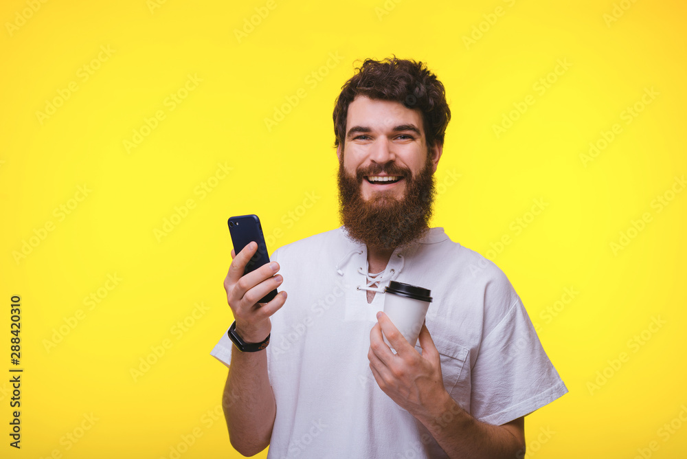 Hnadsome bearded guy holding cup of coffe while using mobile phone Hnadsome bearded guy holding cup of coffe while using mobile phone