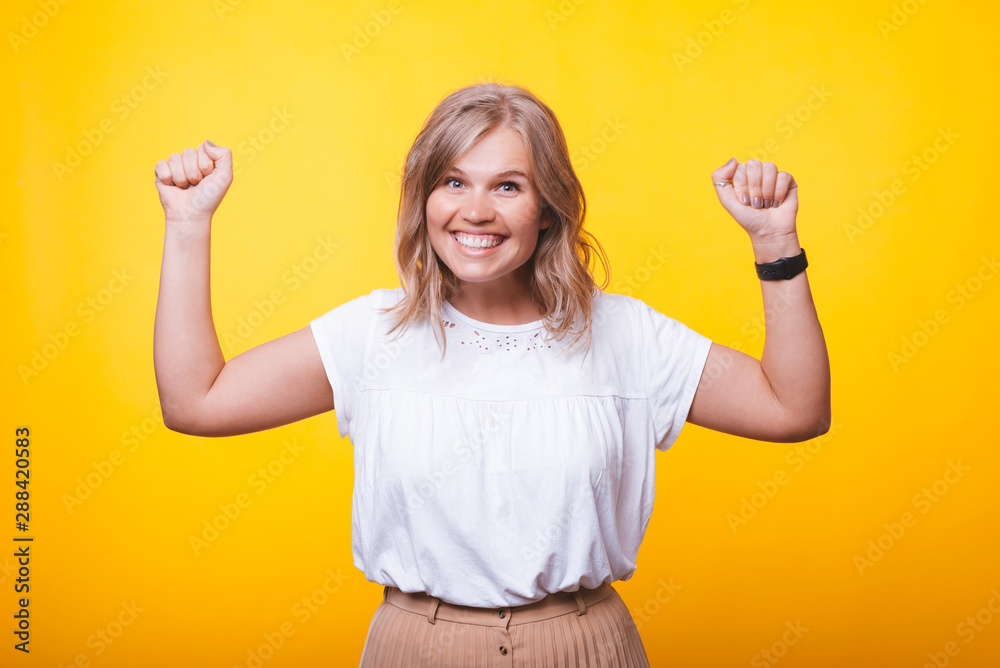 Photo of blonde young winner, celebrating with rised hands over yellow wall Photo of blonde young winner, celebrating with rised hands over yellow wall
