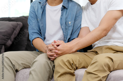Close up of gay man couple holding hands with happiness while sitting in home living room, homosexual and lgbt lifestyle concept