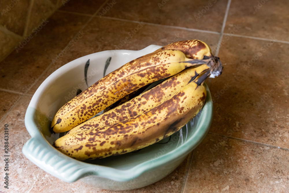 Bunch of very ripe bananas in serving bowl on counter