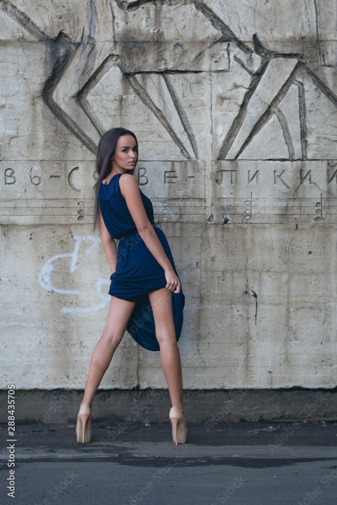 A glamorous woman in a short evening dress with heels stands next to the concrete wall. A glamorous woman in a short evening dress with heels stands next to the concrete wall.