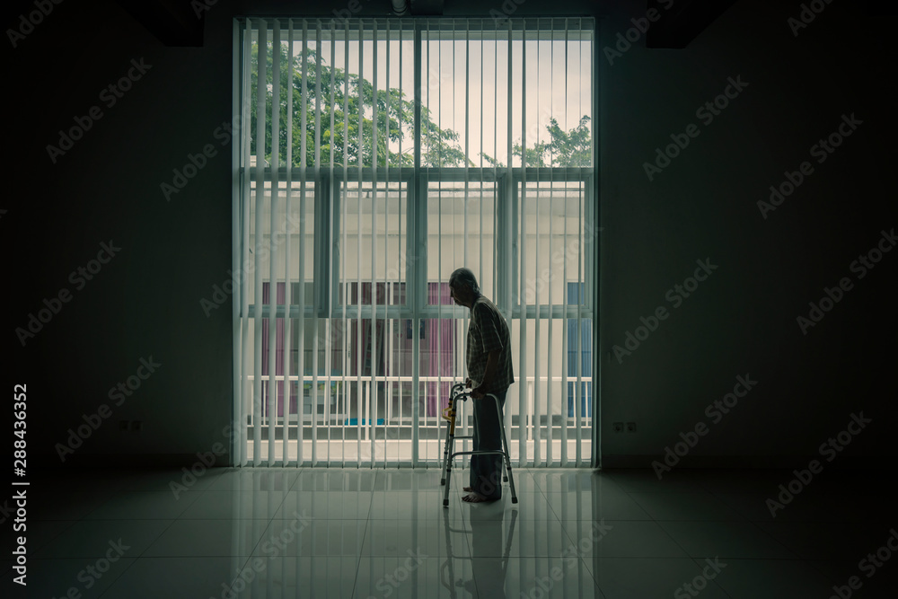 Silhouette of old man walks near the window