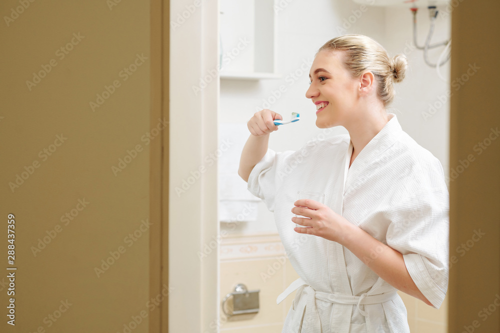 Happy lovely young woman in bath robe brushing teeth in the morning Happy lovely young woman in bath robe brushing teeth in the morning