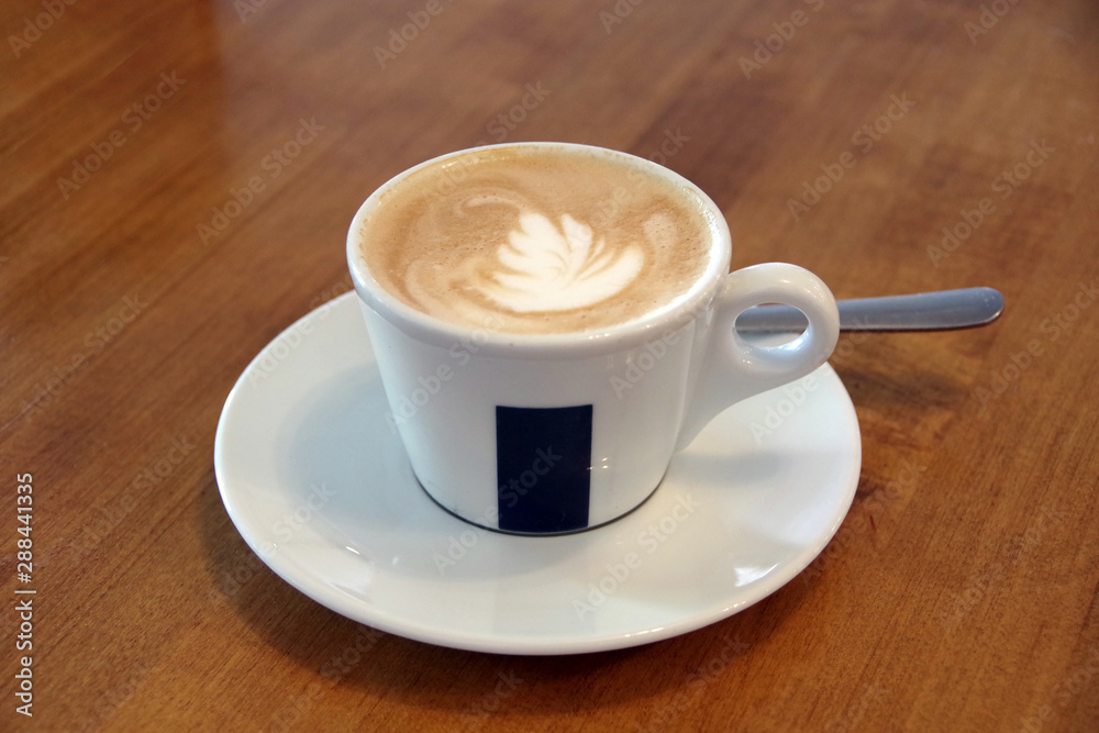 Cappuccino with milk-foam decoration in a white cup on a wooden table
