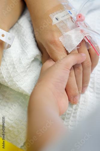 Close-up of kid holding the hand of a woman with IV drip at the hospital