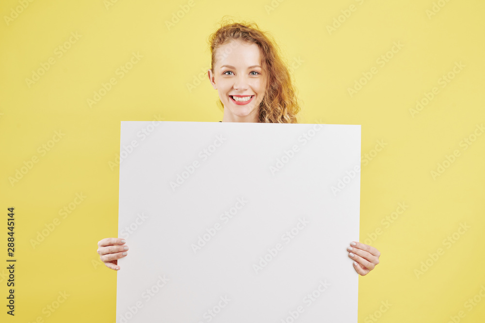 Happy pretty young curly woman holding white empty paper placard Happy pretty young curly woman holding white empty paper placard